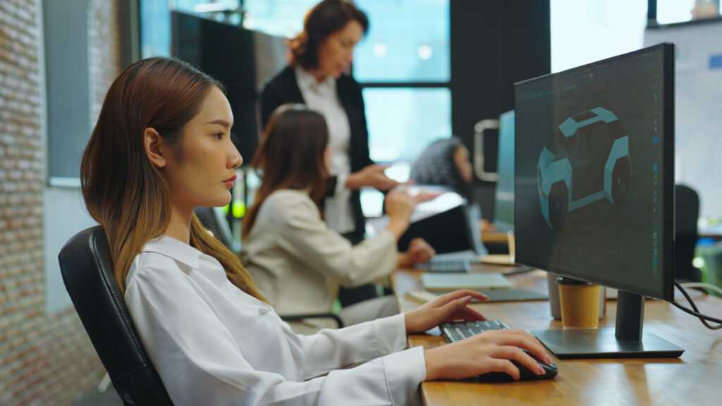 A young Asian woman is designing a 3D electric vehicle at her office, utilizing her knowledge of 3D modeling software which she acquired through her studies in a classroom setting.